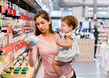 A woman carrying her child looking at a container of food at the grocery store