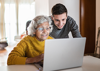 A senior woman looking at her laptop with her grandson looking over her shoulder to help.