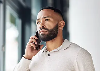 Un hombre que sostiene su teléfono junto a su oreja y luce ligeramente preocupado.