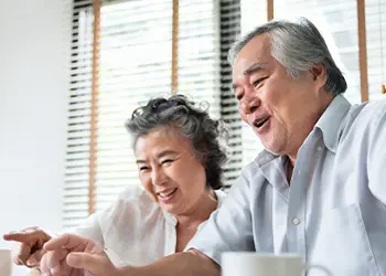 Dos adultos mayores mirando la pantalla de una computadora y sonriendo