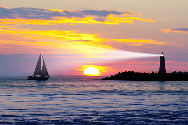 Sailboat and lighthouse during sunset. 