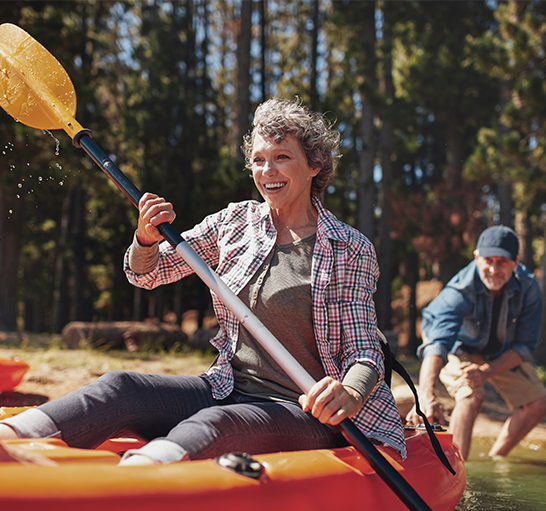 Mature woman kayaking as a man helps push her out from the river bank